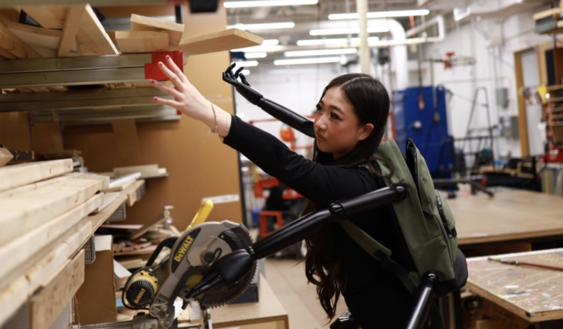 Veronika Wang wearing the ReachOne multi-arm prototype while reaching for lumber on a shop rack
